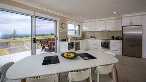 A modern kitchen with white cabinets, a stainless steel refrigerator, and a dining area with a table and chairs. - Peninsula 180, Gerroa, South Coast (Gerroa)