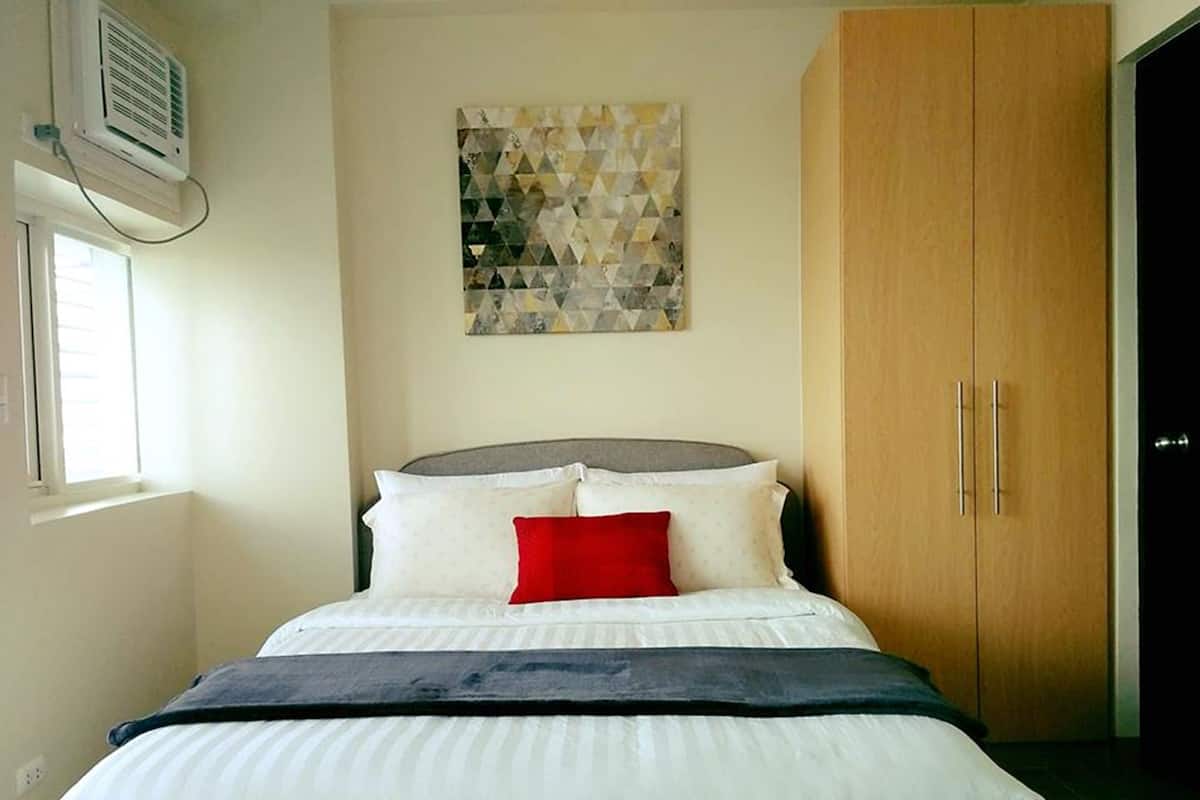 Quarto com cama, janela, ar-condicionado e guarda-roupa de madeira.