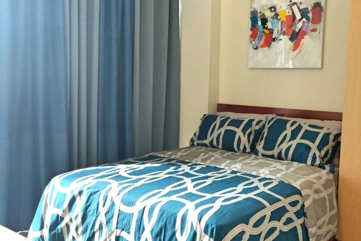 Quarto com cama, cortinas, guarda-roupa e um quadro na parede.