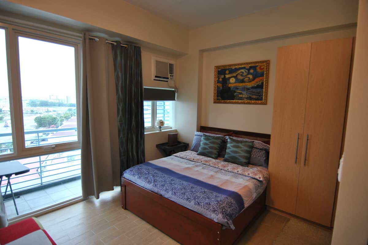 Quarto com cama grande, guarda-roupa, janela com cortinas e um quadro na parede.