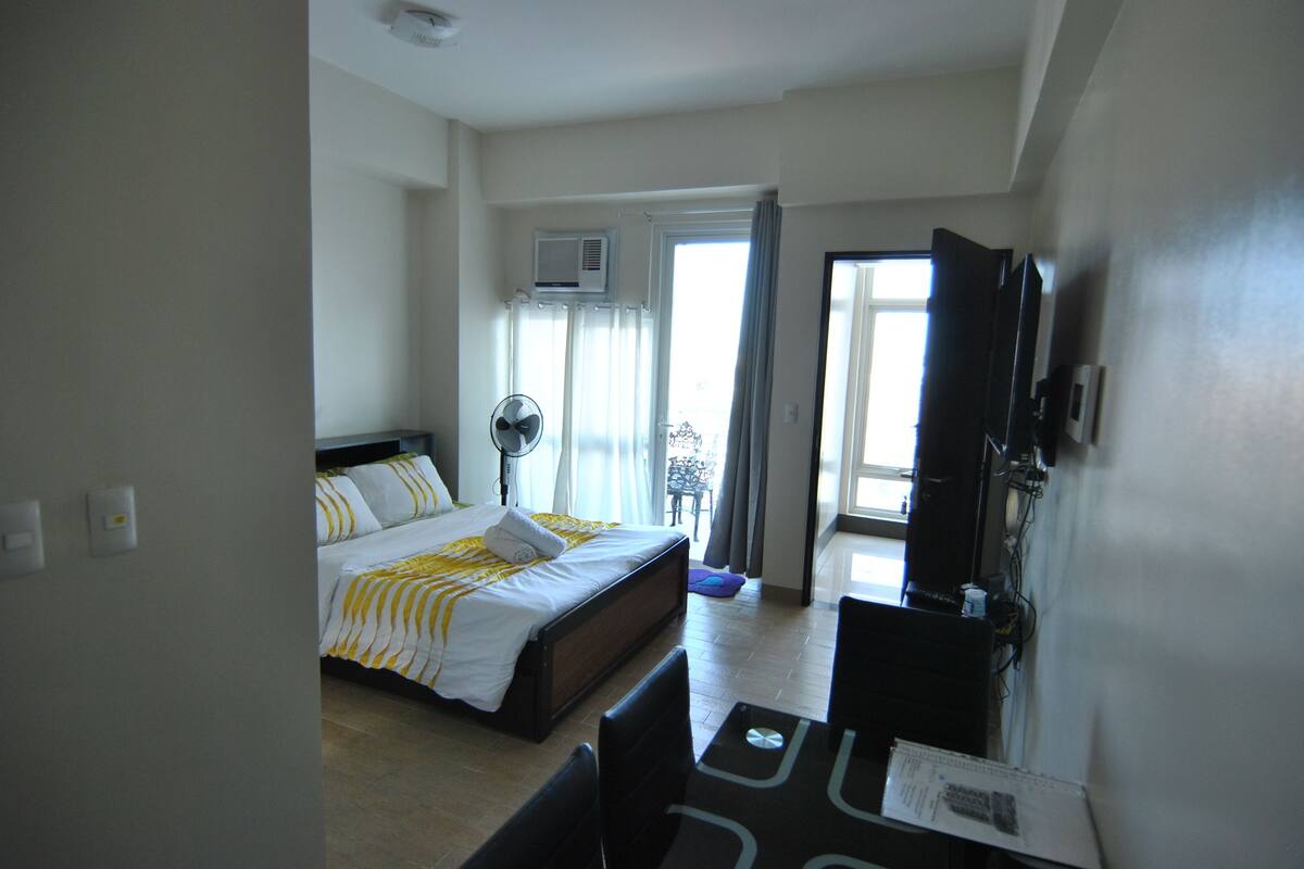 Quarto de hotel com cama, escrivaninha, cadeira, televisão e janela com cortinas.