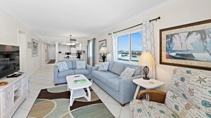 Ein modernes Wohnzimmer mit Sofa, Couchtisch und Fernseher. Ein Fenster bietet Blick ins Freie.