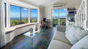 Uma sala de estar espaçosa com uma janela grande, uma mesa de centro de vidro, um sofá e uma varanda com vista para o campo.