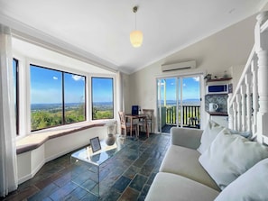 A spacious living room with a large window, a glass coffee table, a sofa, and a balcony with a view of the countryside. - Villa 4 @ Bimbadeen Estate - Split level villa with sensational views all around - just for 2! (Mount View)