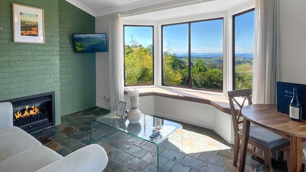 Uma sala de estar com lareira, mesa de centro de vidro, sofá, mesa de jantar e uma grande janela com vista panorâmica.
