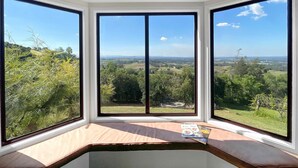 Quarto com três amplas janelas com vista para uma paisagem verde.