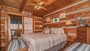 Un dormitorio rústico de madera con una cama grande, una mesita de noche, un aparador y un ventilador de techo.
