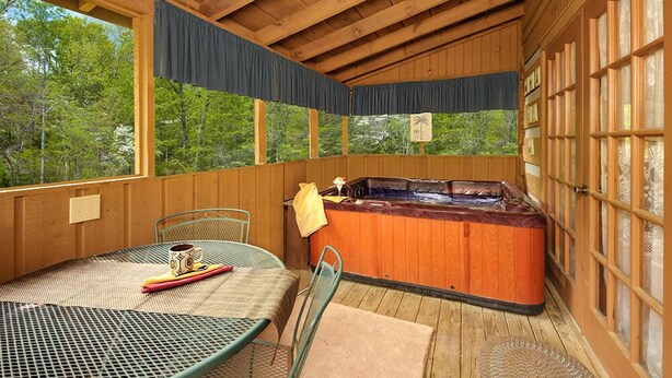 Una terraza de madera con un jacuzzi, una mesa con sillas y vistas al bosque.