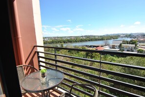 A balcony with a glass table and chairs, overlooking a river and cityscape. - The Uptown Place (Iloilo)