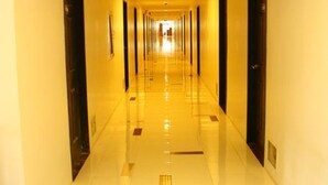 Un long couloir d’hôtel, bien éclairé, avec des portes de chaque côté et un sol carrelé brillant.