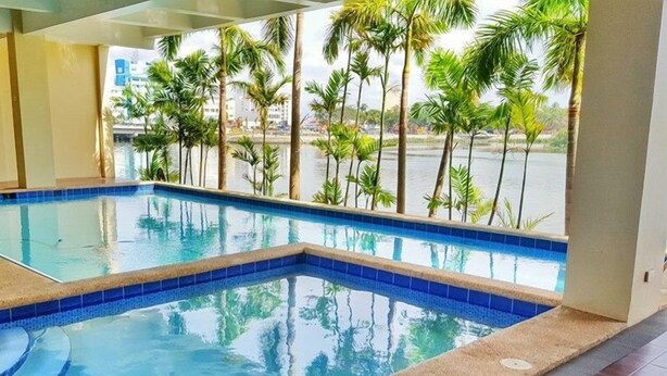 Une piscine intérieure à l’eau d’un bleu cristallin, entourée de palmiers et offrant une vue sur une étendue d’eau.