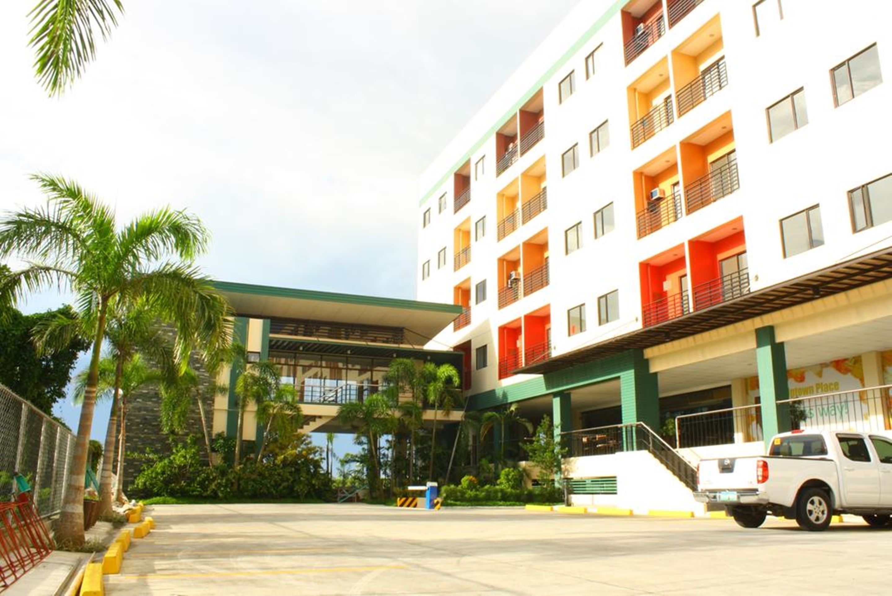 Hotel com vários andares, varandas, estacionamento e palmeiras.