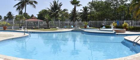 A swimming pool with a tiled deck, palm trees, and a fenced area.