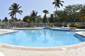 Una piscina con cubierta de baldosas, palmeras y un área delimitada por una valla.