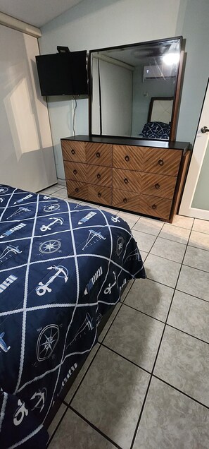 Un dormitorio con cama, cómoda, televisor montado en la pared y espejo sobre la cómoda.