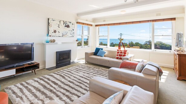 A living room with a flat-screen TV, fireplace, sofa, and large windows with a view of the sea. - BEACH BELLE - MORNINGTON (MORNINGTON)