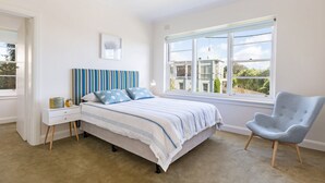 A bedroom with a bed, a chair, a nightstand, a window, and a framed picture on the wall. - BEACH BELLE - MORNINGTON (MORNINGTON)