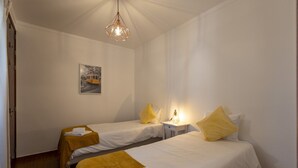 Ein Hotelzimmer mit zwei Betten, jedes mit einem gelben Kissen und einem weißen Handtuch. An der Wand hängt ein Gemälde und eine Pendelleuchte.