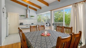 Une cuisine moderne avec un coin repas, des poutres en bois et une vue sur la verdure environnante.