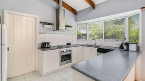 Une cuisine moderne avec des meubles blancs, un four encastré, une plaque de cuisson et une grande fenêtre équipée de stores.