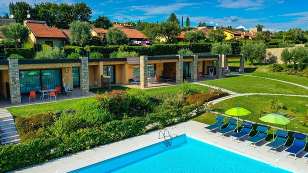 A modern pool area with lounge chairs and umbrellas, surrounded by well-maintained gardens and a view of residential buildings.