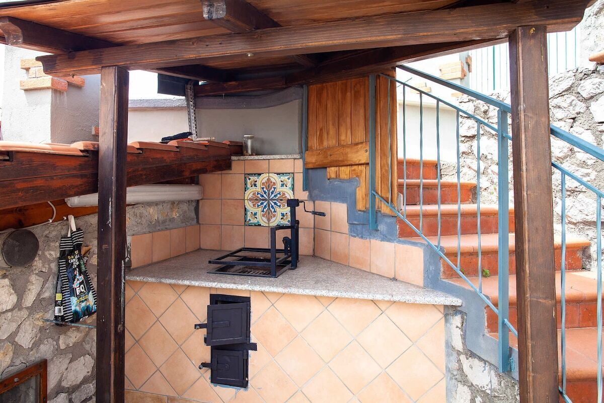 A small outdoor kitchen area with a tiled backsplash, a built-in oven, and a wooden pergola overhead.