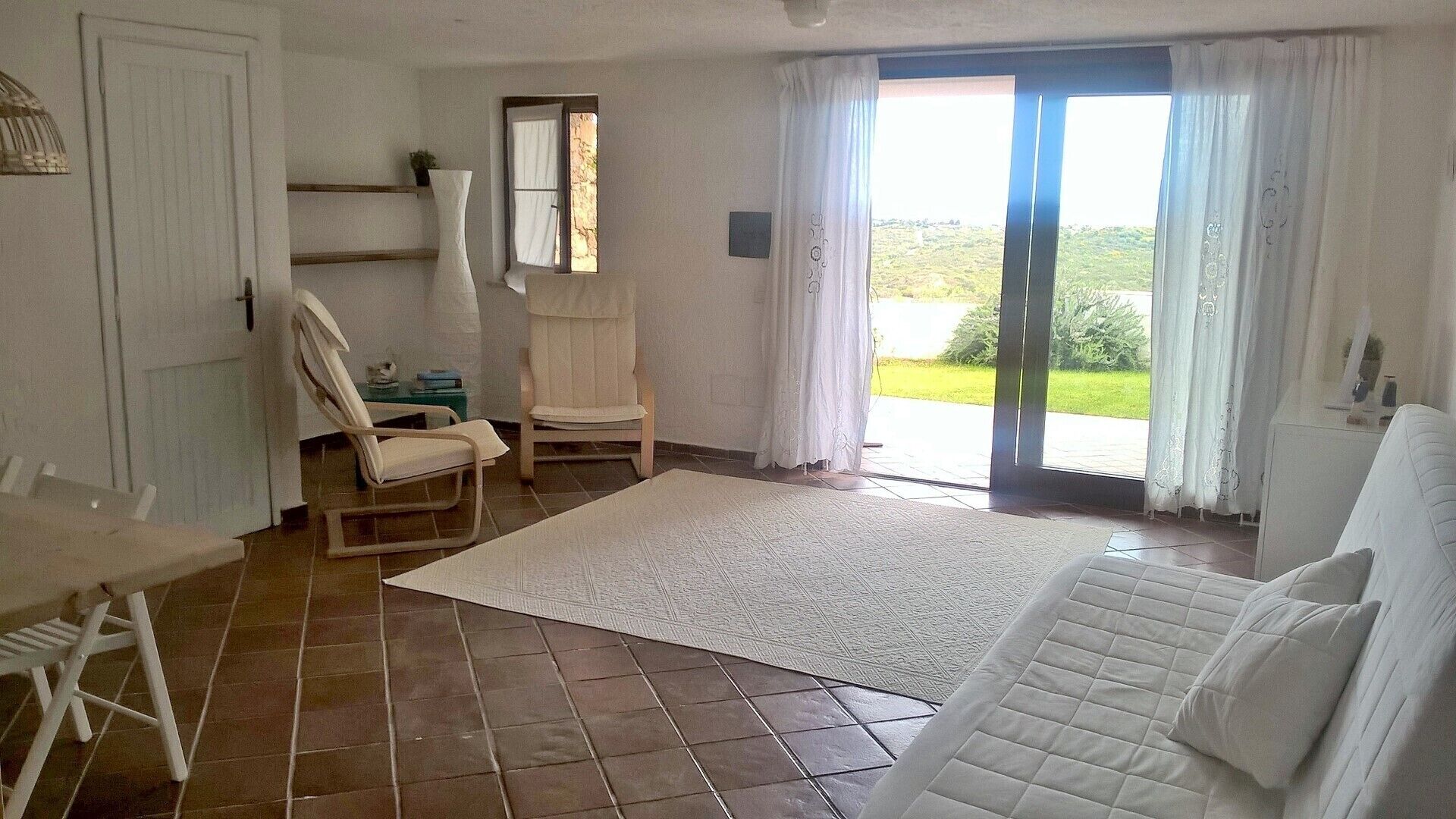 A room with a large window, a white sofa, a chair, and a small table.