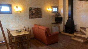 A cozy living room with a wooden dining table, a red sofa, a fireplace, and a painting on the wall. - Rural apartment L'Alzina for 2 people (Tavertet)