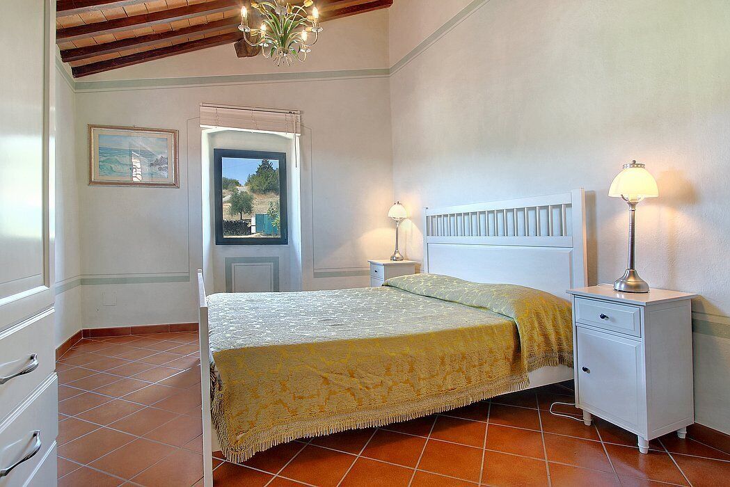 A bedroom with a bed, bedside tables, a window with a view, and a chandelier.