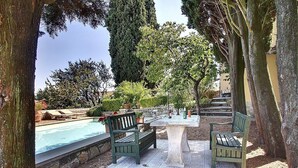 Ein Poolbereich mit einem Steintisch, zwei Bänken und Blick auf Pool und Garten.