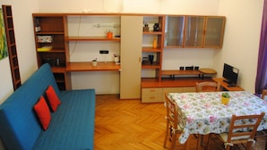 A compact living space with a blue sofa, a dining table with chairs, a wooden desk, and a bookshelf. - San Raffaele Città Studi Politecnico CIN IT015146C2F3B9XNN (Milano)