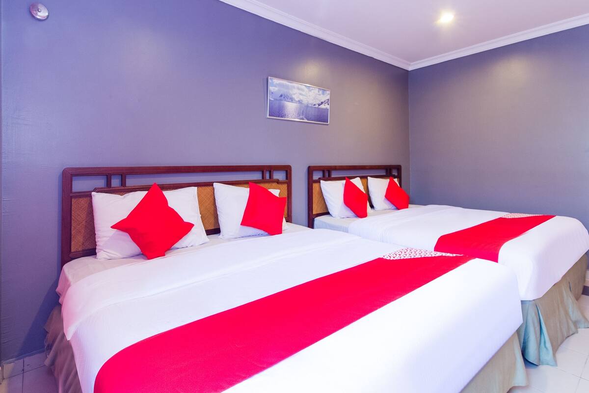 A hotel room with two beds, each with white bedding and red accents, a small painting on the wall, and a ceiling light.