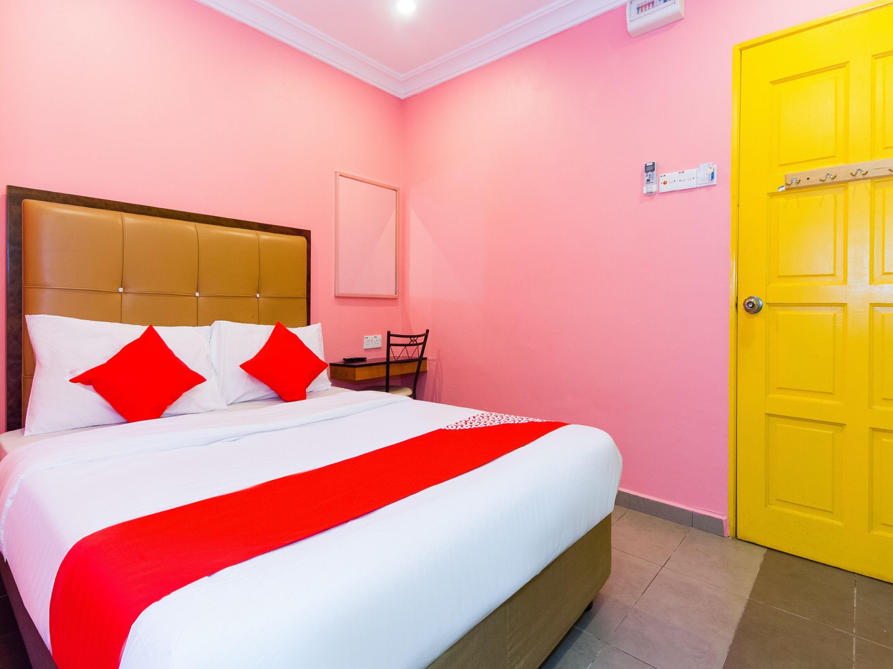 A hotel room with a bed, a chair, a desk, and a yellow door.