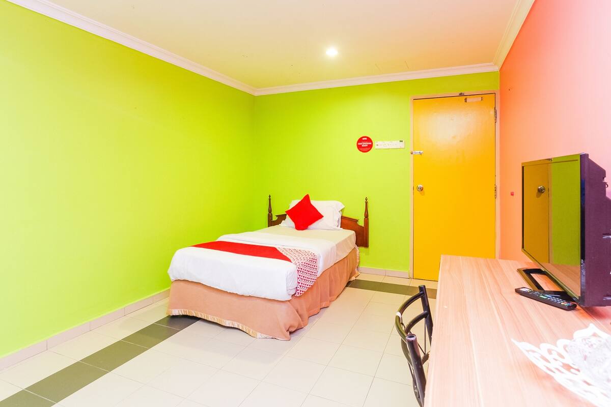 A hotel room with a bed, a television, and a door with a red sign.