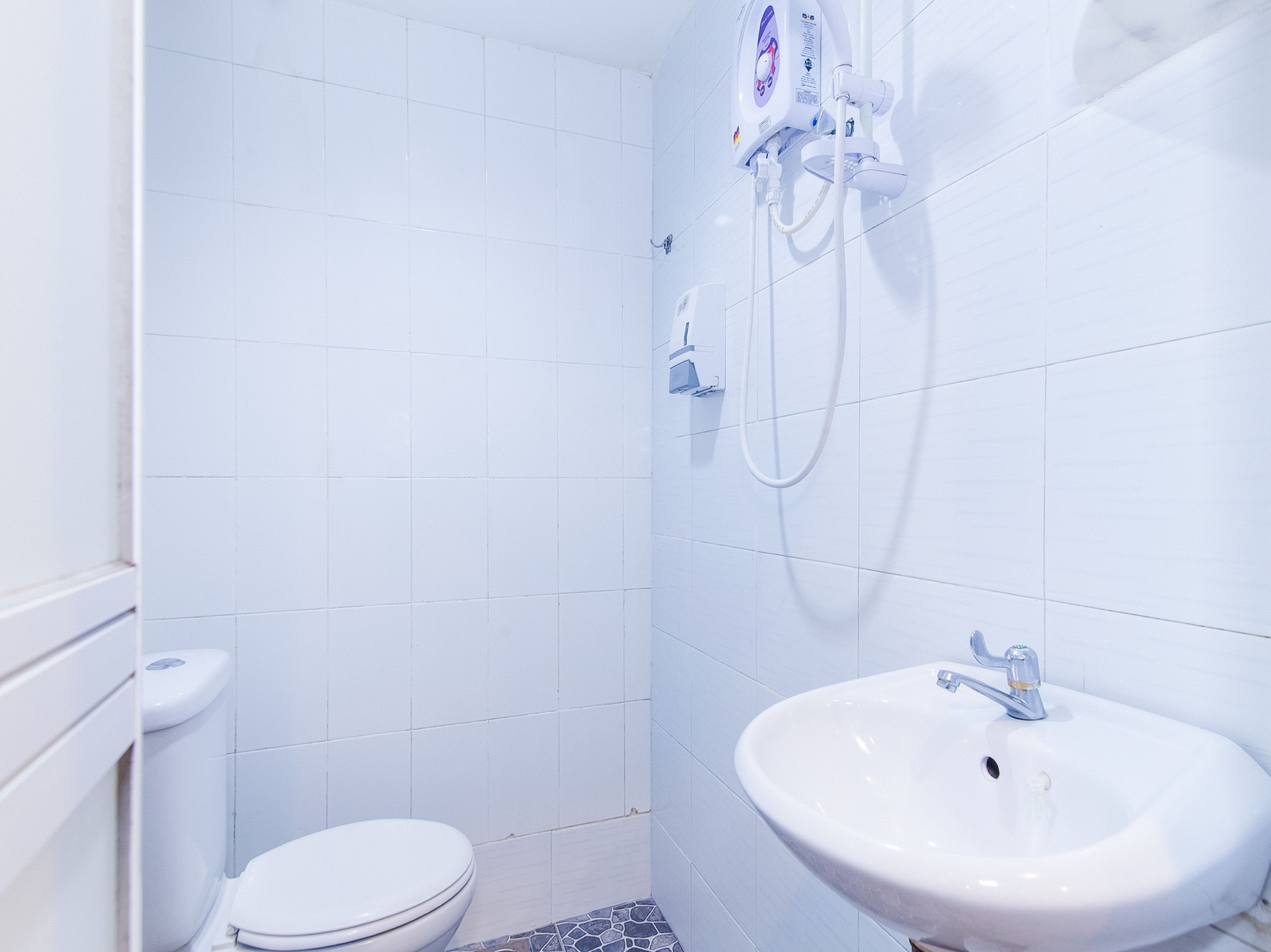 A bathroom with white tiles, a toilet, a sink, and a shower unit.