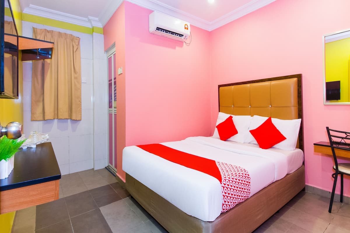 A hotel room with a bed, a desk, a chair, and an air conditioning unit.