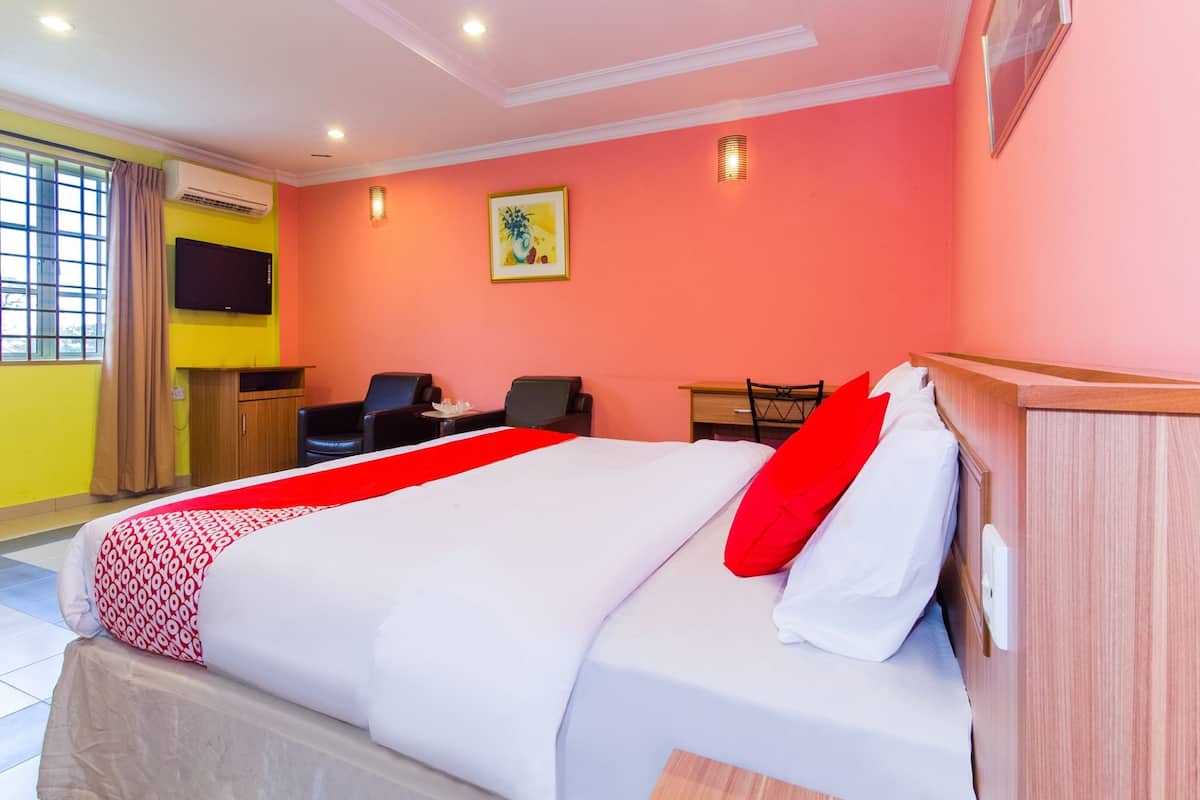A hotel room with a bed, a desk, two chairs, a TV, and a window with curtains.