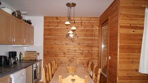 Comedor con paneles de madera, mesa dispuesta para seis comensales, cafetera y lavavajillas en la cocina contigua.