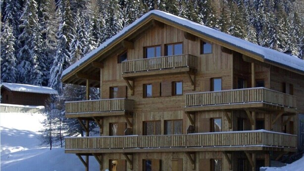 Una cabaña de madera con varios balcones, rodeada de árboles cubiertos de nieve.