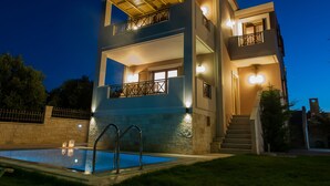 Un moderno edificio de dos pisos con piscina, balcones e iluminación exterior.