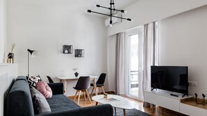 A modern living room with a sofa, a coffee table, a TV, and a dining area with chairs and a table. - UPSTREET Desirable 1BD Apt in Kolonaki (Athens)