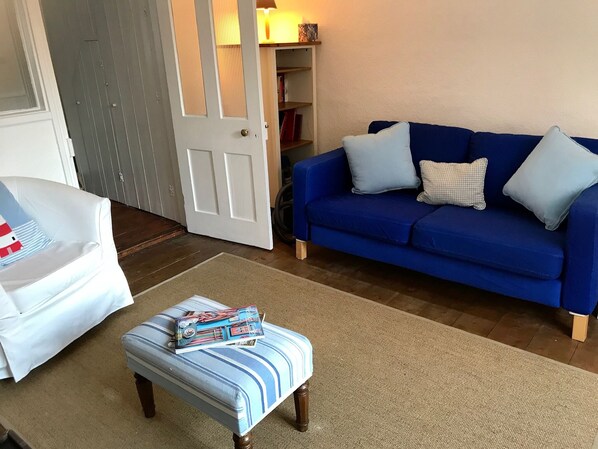 Un salon avec un canapé bleu, un fauteuil blanc et un pouf à rayures.