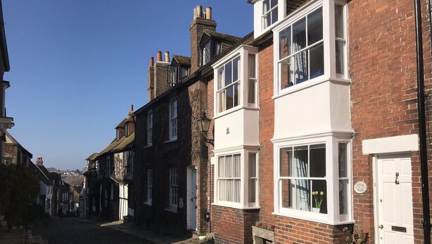 A narrow cobblestone street lined with traditional brick houses, featuring white-framed windows and a mix of brick and timber construction. - Pretty 18th century cottage centrally situated  on Mermaid Street in Rye (Rye)