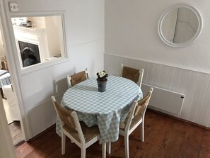 Un coin repas avec une table ronde recouverte d’une nappe à carreaux, entourée de quatre chaises en osier.