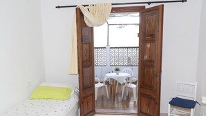 Une chambre avec un lit, une chaise, une table et un balcon agrémenté d’une balustrade décorée.