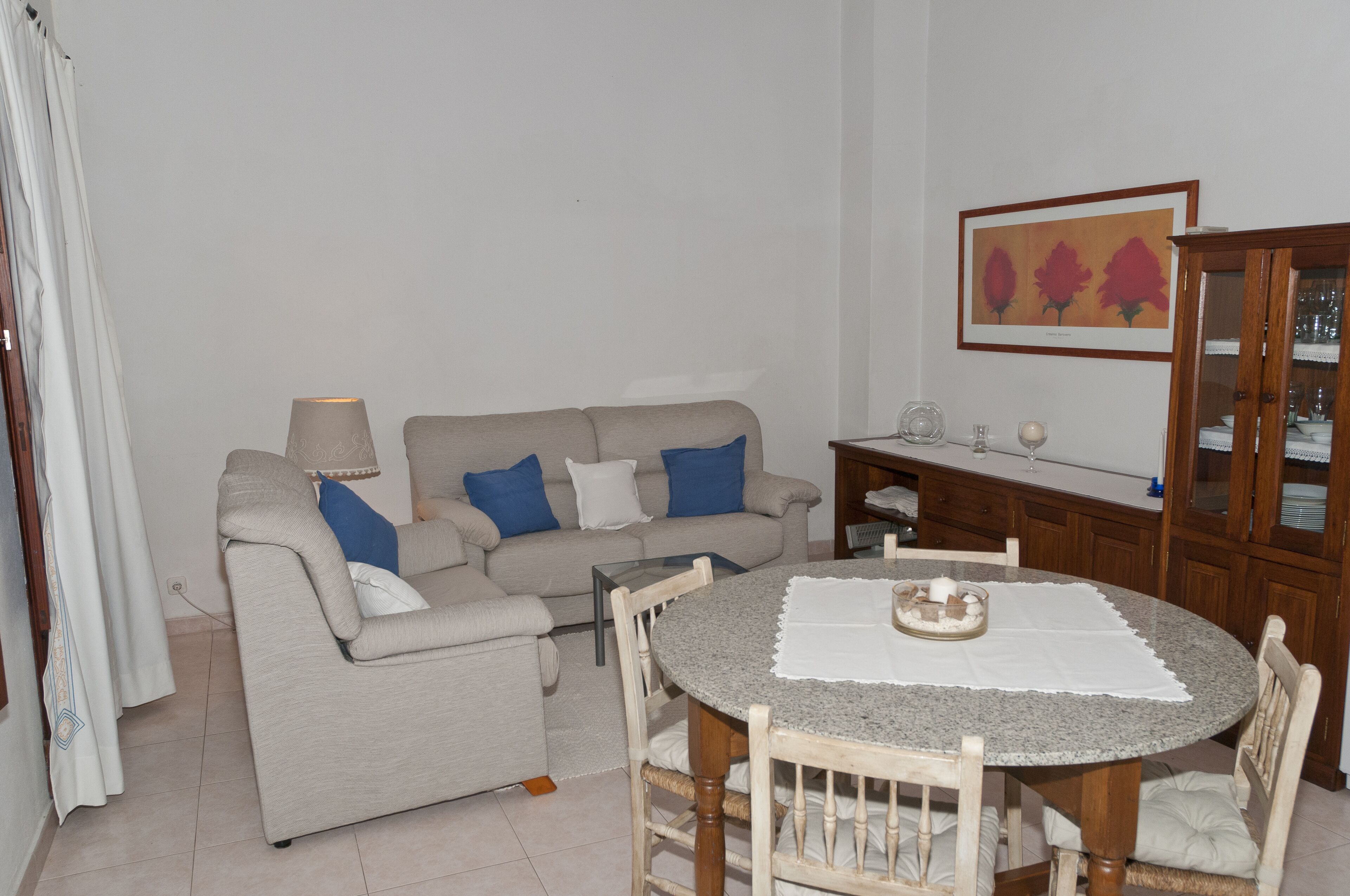 A living room with a sofa, a dining table with chairs, a lamp, and a framed picture on the wall.
