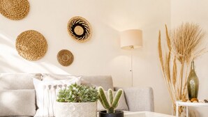 A living room with a sofa, two potted plants, a lamp, and decorative wall hangings. - ⭐️⭐️⭐️⭐️⭐️AMAZING BEACH HOUSE in TINOS! Literally On the Beach!  (Tinos)