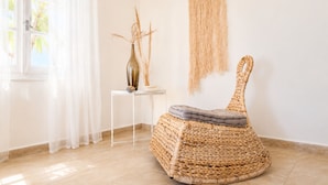 A room with a wicker chair, a small table with a vase, and a wall hanging. - ⭐️⭐️⭐️⭐️⭐️AMAZING BEACH HOUSE in TINOS! Literally On the Beach!  (Tinos)