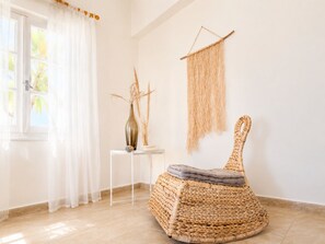 Une pièce comprenant un fauteuil en osier, une petite table avec un vase et une décoration murale.