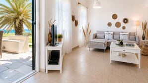 A modern living room with a sofa, coffee table, and TV stand, a balcony with a palm tree, and a view of the sea. - ⭐️⭐️⭐️⭐️⭐️AMAZING BEACH HOUSE in TINOS! Literally On the Beach!  (Tinos)